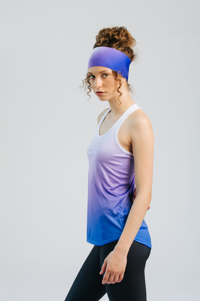 A woman models a white, purple, and blue gradient racerback sports top and a matching headband. Sieviete demonstrē baltu, violetu un zilu gradienta sporta topu ar racerback stila muguru un pieskaņotu galvas saiti."
