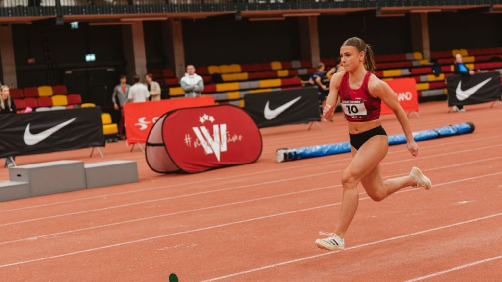 A female sprinter competing in a personalized maroon athletic top. This custom sportswear demonstrates professional sublimation printing and vibrant colors, designed for durability and comfort during high-intensity track events.