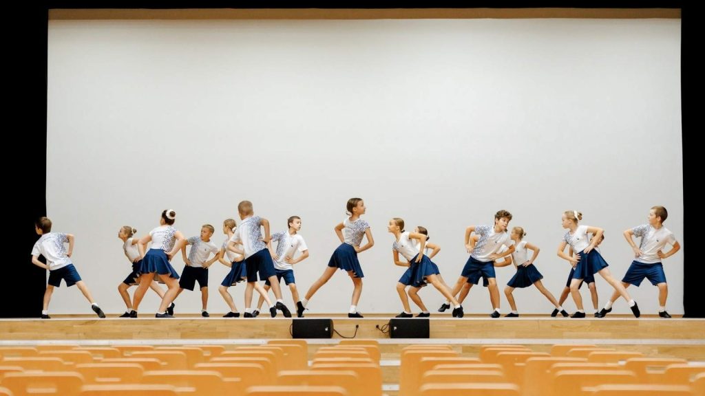 Zelta Sietiņš dance group performs in custom dance wear, featuring matching navy-patterned white shirts and bodies and coordinated blue skirts and shorts.