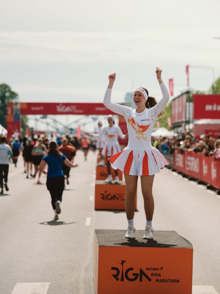 A woman wearing custom sportswear cheers for runners during a Rimi Riga Marathon event.