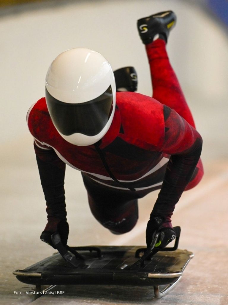 An action shot of an elite athlete in a custom teamwear skeleton speed suit navigating an ice track, showcasing the aerodynamic performance and high-definition sublimation on specialized technical fabric.