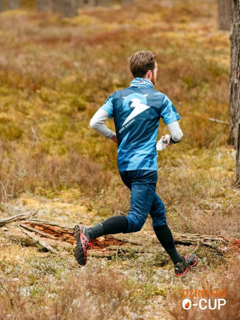 An orienteering runner wearing a custom sportswear jersey with sublimation print features clean graphics while running through a forest trail.