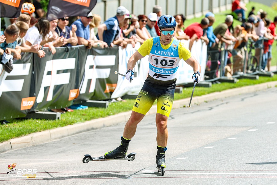 Male athlete in custom yellow and green rollerskiing sportswear crossing the finish line in Latvia.