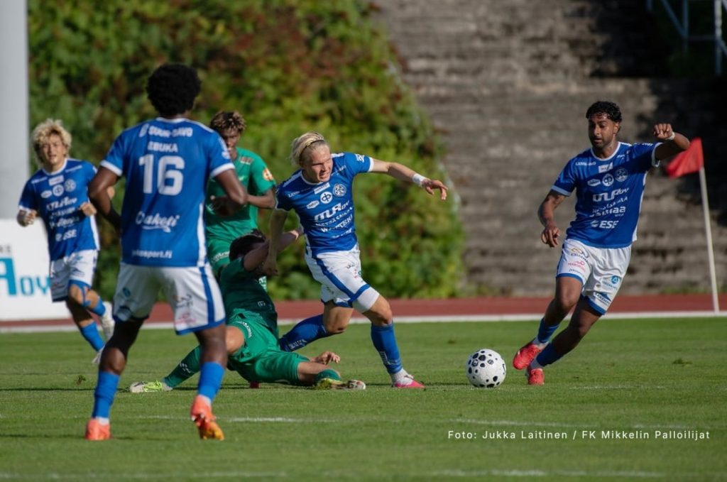 Action shot of multiple Mikkelin Palloilijat football players competing on the pitch in blue and white custom made team uniforms.