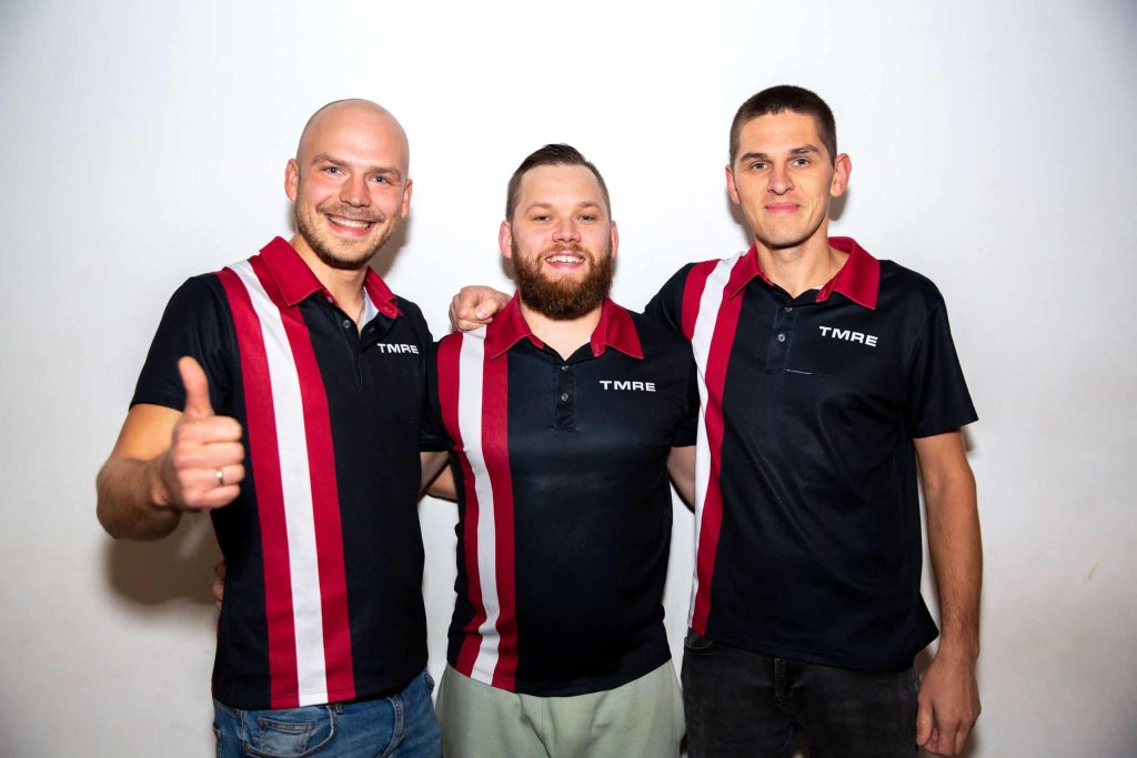 Three male members of the TMRE bowling team posing together in custom sublimated black polo shirts with red and white vertical stripes.