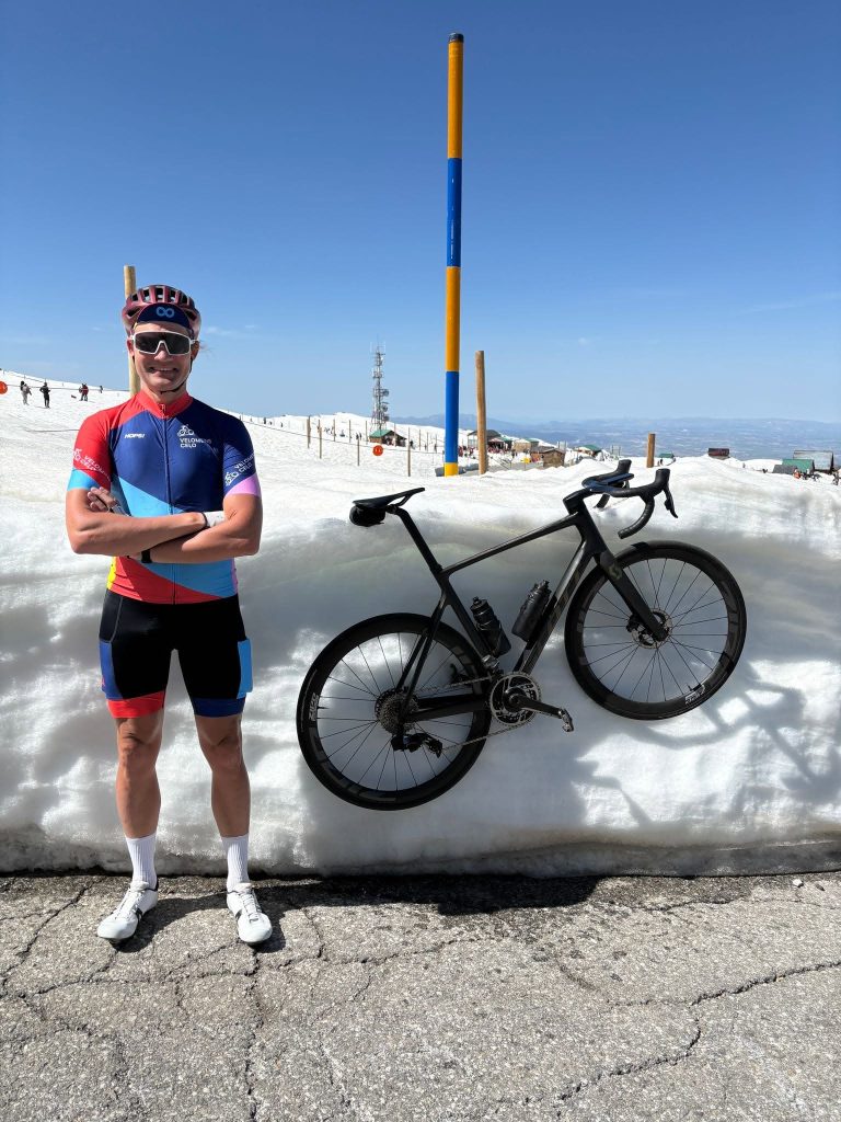 Cyclist in custom colorful Velomens Ceļo cycling kit with road bike on a mountain pass.