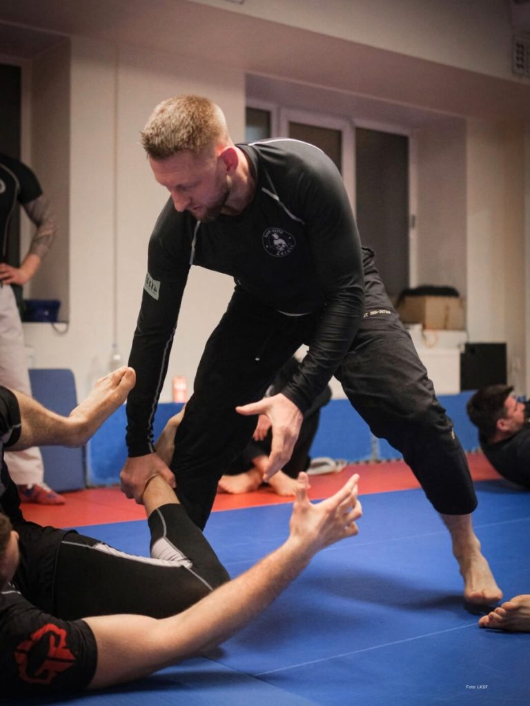 Džiu-džitsu sportists treniņā, ģērbies funkcionālā kreklā ar garām piedurknēm un personalizētu apdruku.